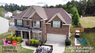 A two-story brick house with a large driveway and greenery around it.