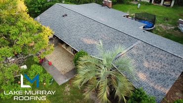 Aerial view of a house with a newly installed roof surrounded by trees and a trampoline.