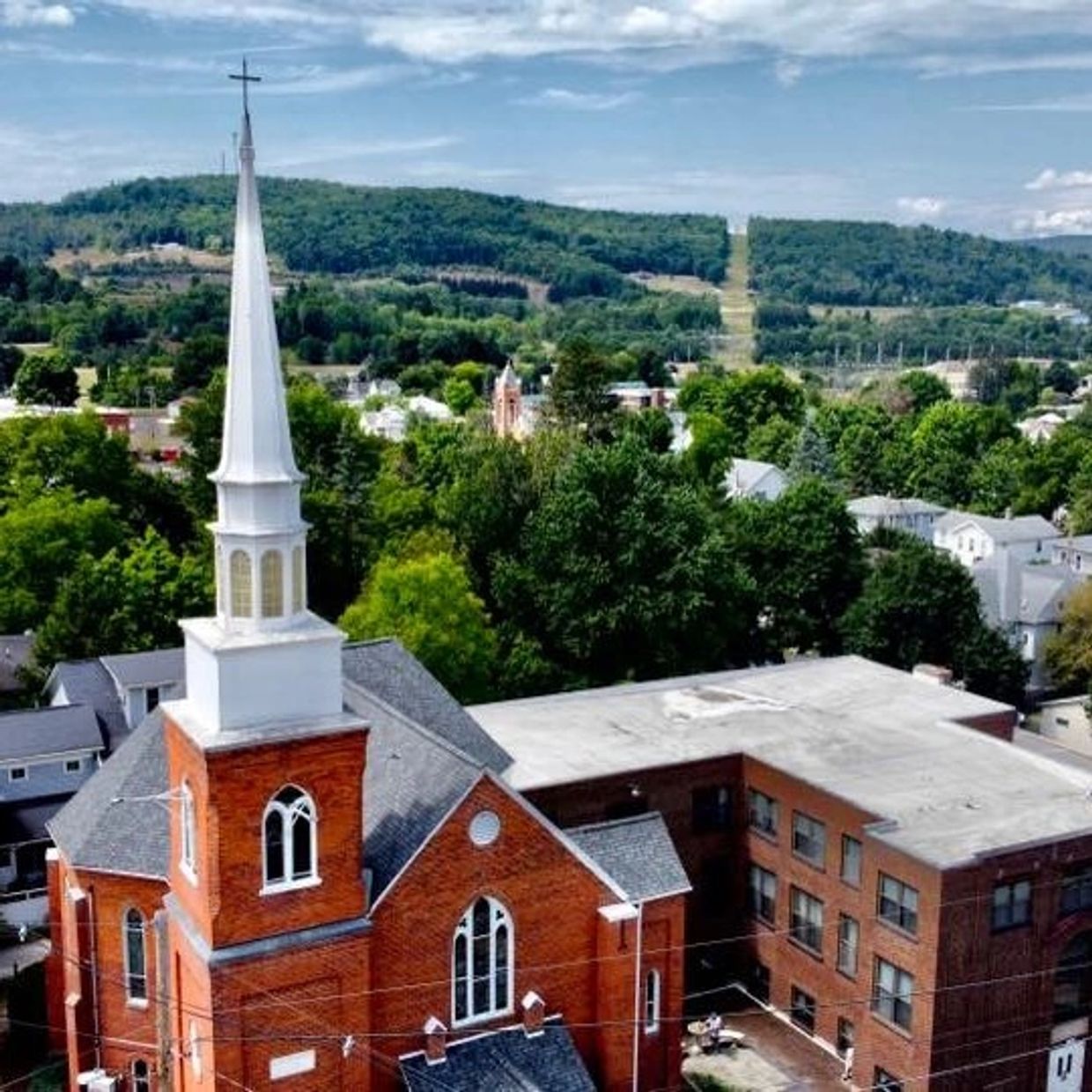 Red brick church with a tall white steeple in a green town.
