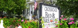 Sign for Crossroads Bed &amp; Breakfast surrounded by flowers.