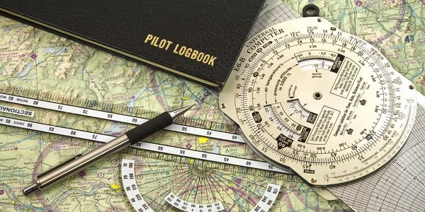 Pilot logbook, navigation plotters, and flight computer on aviation map.