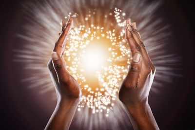 Hands hovering over an open book with magical sparkles rising.