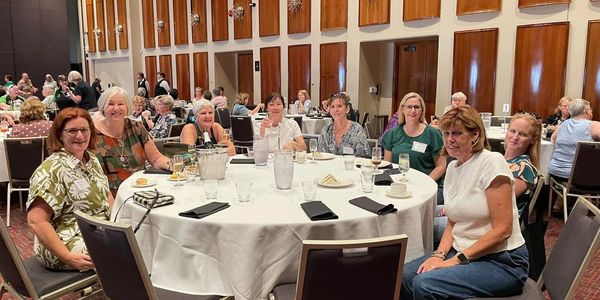 Group of women sitting around a banquet table in a large event hall.