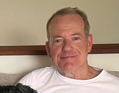 Smiling man sitting indoors, wearing a white t-shirt.