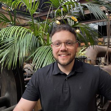 Smiling man with glasses in a lush, industrial indoor setting.