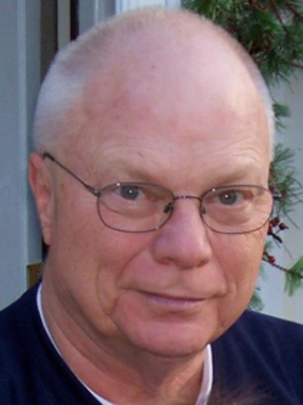Elderly man with glasses looking at the camera outdoors.
