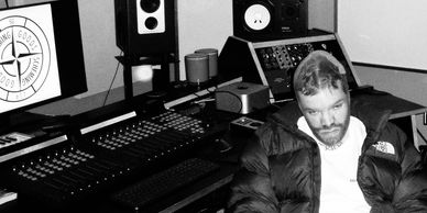 Man sitting in a music studio surrounded by audio equipment.
