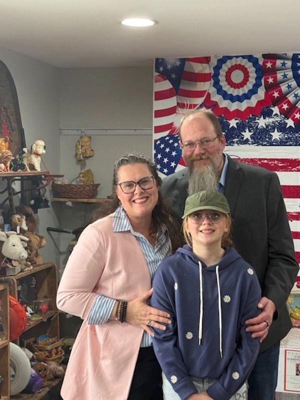 A smiling family of three posing indoors with patriotic decorations.