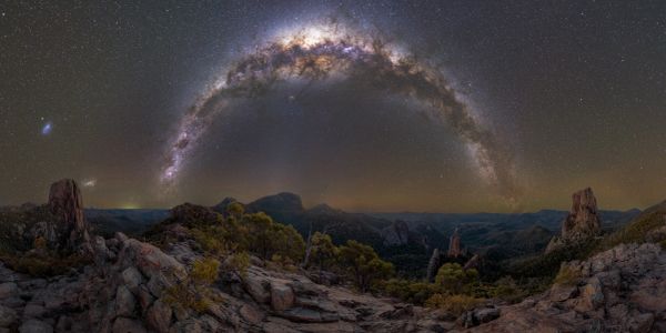 Milky Way arch over rocky landscape at night.