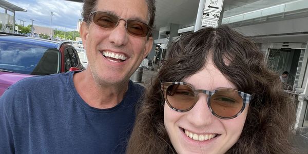 Two people smiling outdoors, wearing sunglasses.