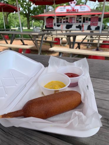 Alt="Corndog, ketchup, and mustard on a picnic table at MooSa's North Point"