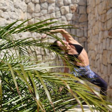 Person doing yoga stretch near stone wall and plants.