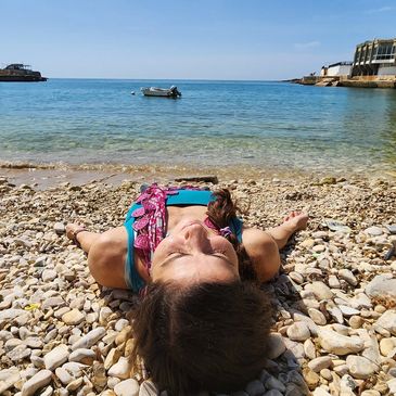 Person lying on a pebble beach soaking up the sun.