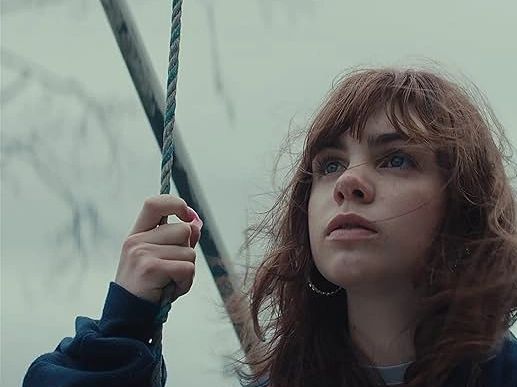 A young woman holding onto ropes, looking thoughtfully into the distance.