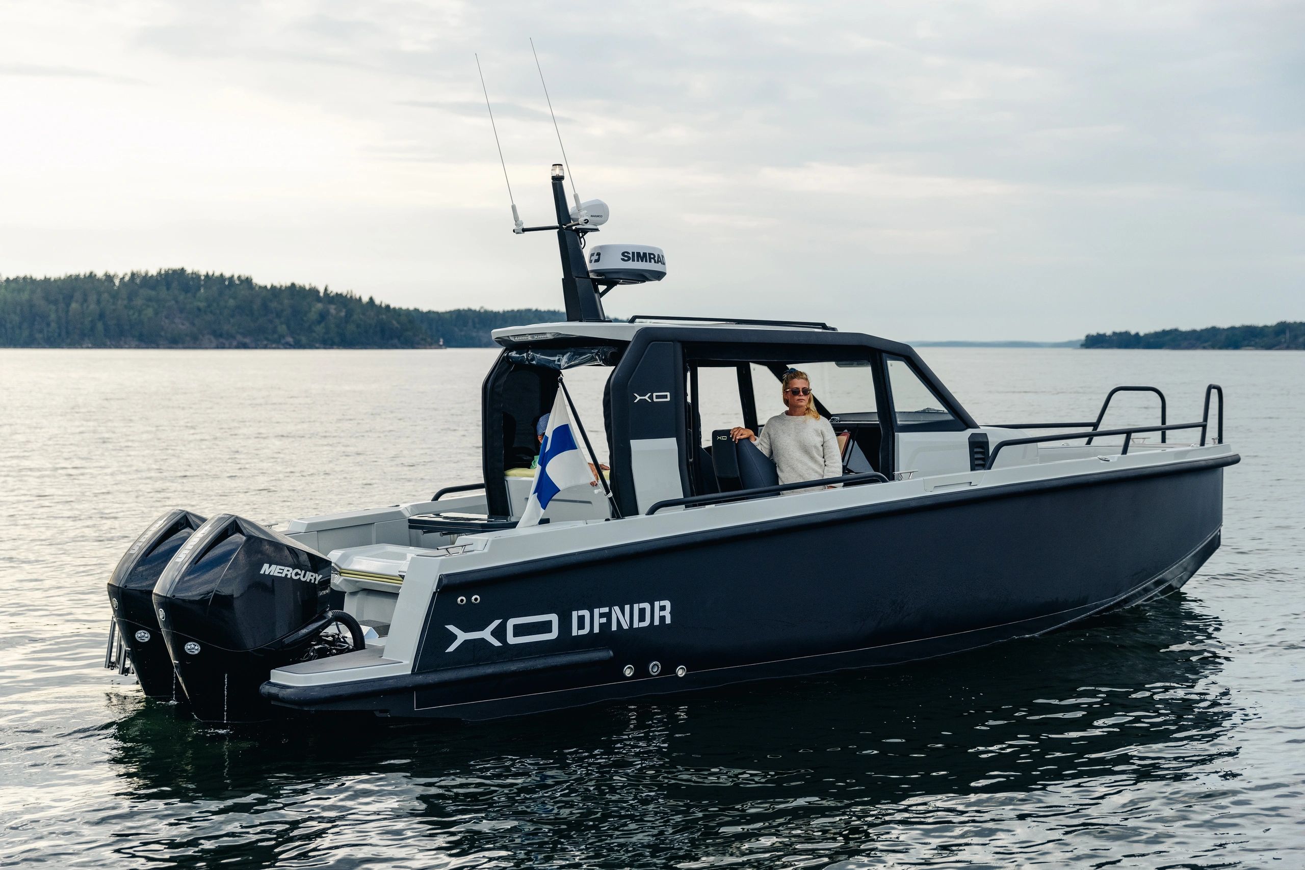 A woman standing on a sleek black XO DFNDR boat on calm waters.