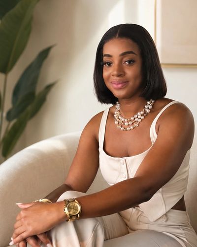 Confident woman in a white outfit sitting gracefully indoors.