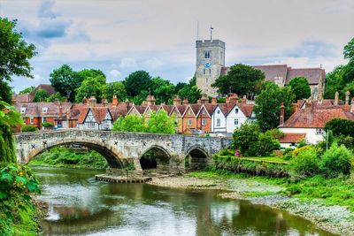 A scenic view of a stone bridge over a river with historic houses and a church tower in the background.