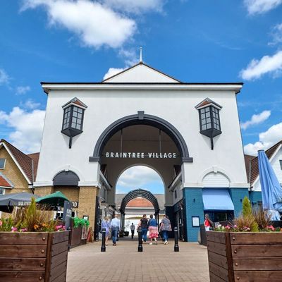 Entrance archway to Braintree Village shopping center under a blue sky.