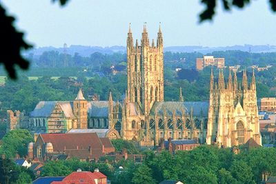 A grand cathedral with tall spires amidst lush greenery in a city.