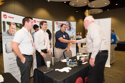Business professionals shaking hands at a company booth during a networking event.