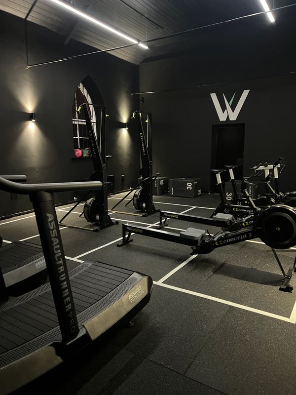 Modern gym with rowing machines and treadmills in a dimly lit room.