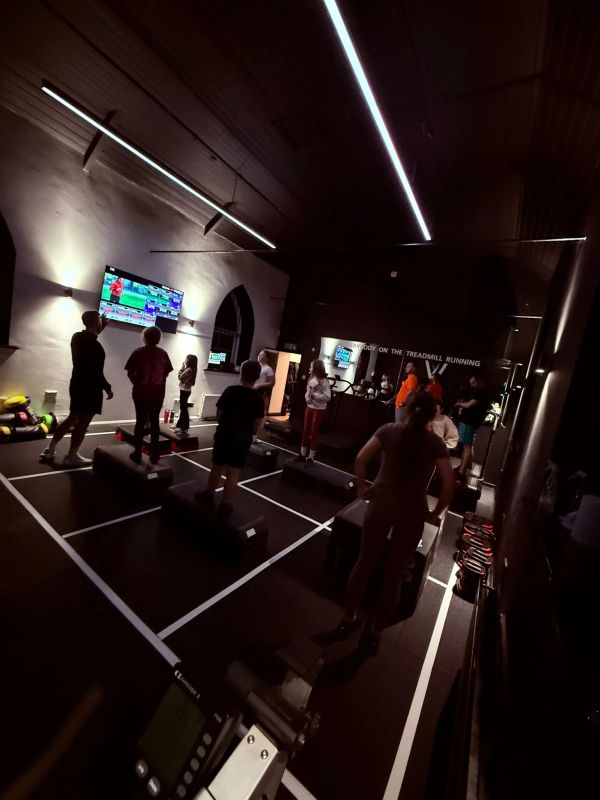 Group workout session in a dimly lit gym with step platforms and screens.