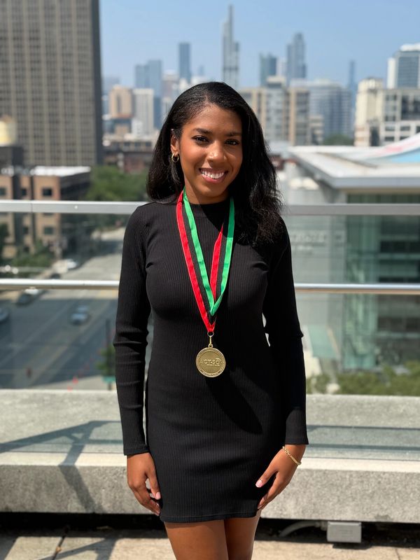 Woman smiling with a medal around her neck in an urban setting.