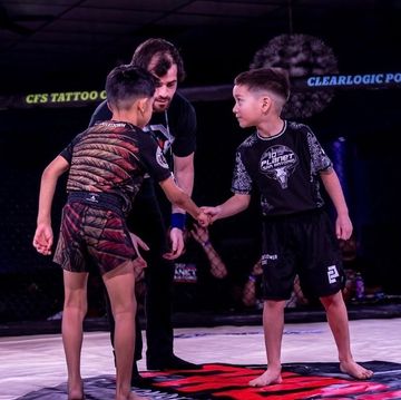 Two young martial artists shake hands before a match in a ring.