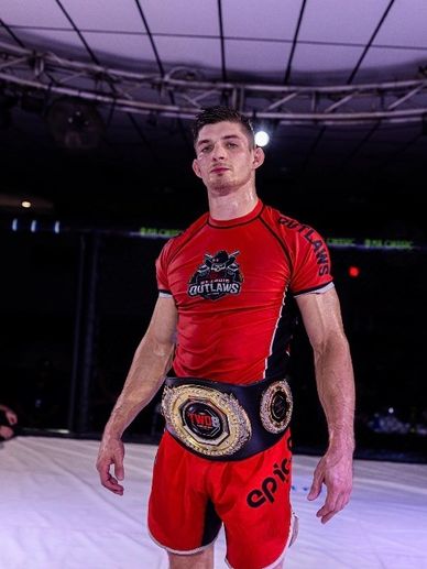 Martial artist with championship belt in fighting ring.