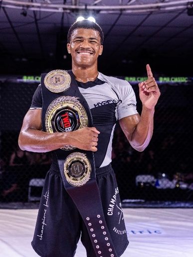 Smiling MMA champion holding a title belt and showing number one.