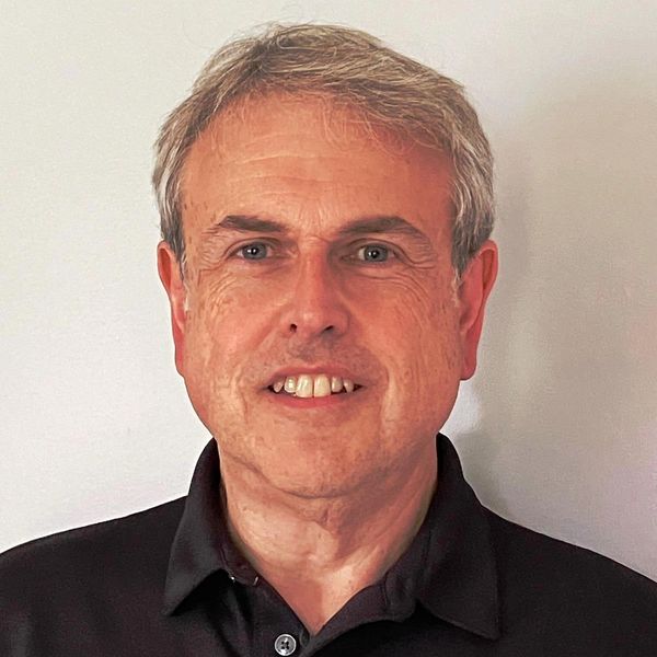 Portrait of a middle-aged man with gray hair wearing a black polo shirt.