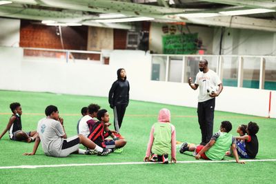 Coach instructing young soccer players sitting on an indoor field.
