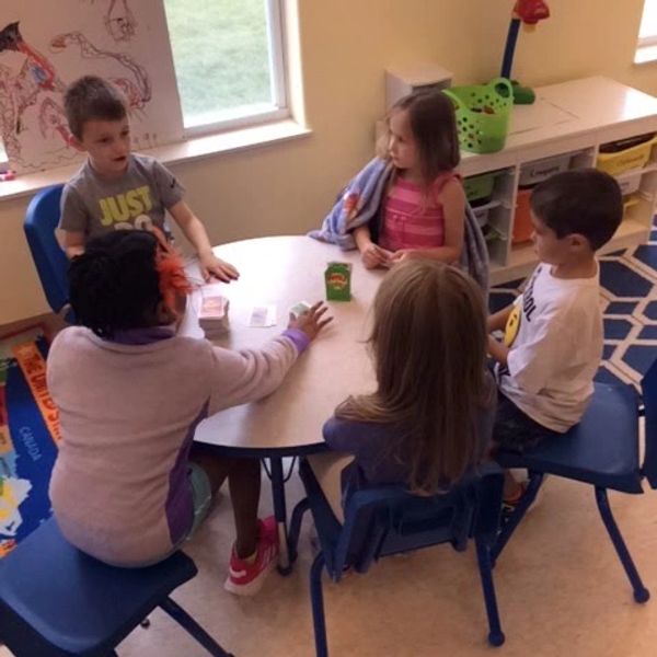 Young children sitting around a classroom table playing card games and engaging in conversation.