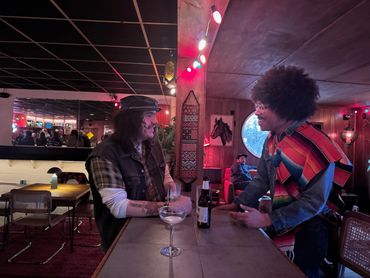 Two men chatting happily at a cozy bar with colorful lighting.