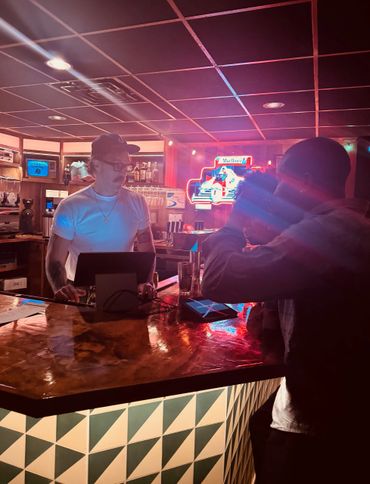 Bartender wearing a mask stands behind a bar counter at a dimly lit bar.
