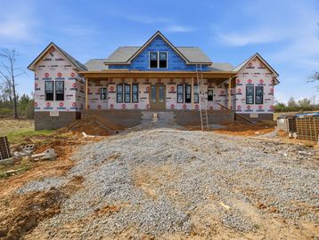 A house under construction with a gravel driveway and blue sky.