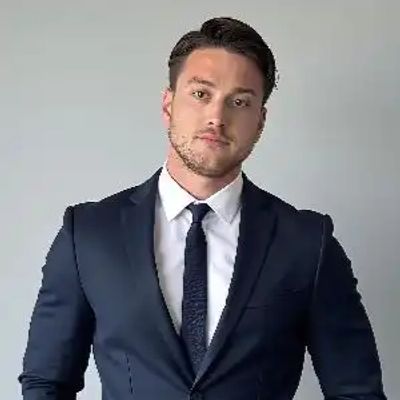 A man in a navy suit and tie posing against a plain background.
