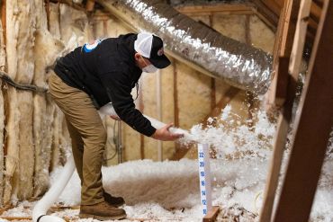 Worker installing loose-fill insulation in an attic.