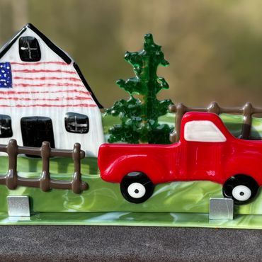 A decorative scene with a barn, red truck, and tree on a glass base.