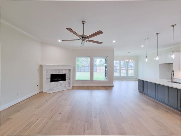 Vacant open-plan living room with pale wood floors, a fireplace, ceiling fan, and kitchen island