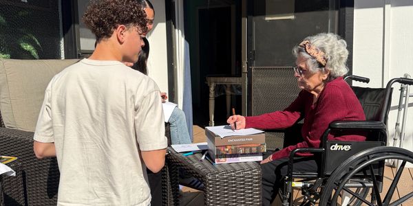 A young person and an elderly woman in a wheelchair engaged in writing outdoors.