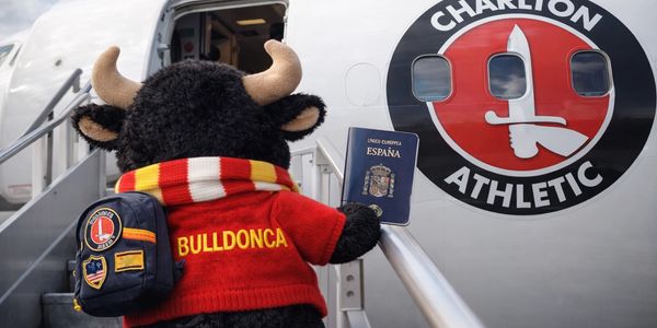 A bull mascot holding a Spanish passport boarding a plane with Charlton Athletic logo.