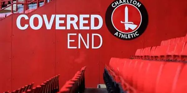 Red stadium seats near a wall with 'Covered End' and Charlton Athletic logo.