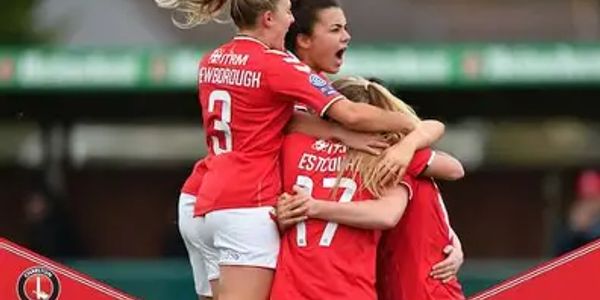 Female soccer players in red jerseys celebrating a goal with a group hug.