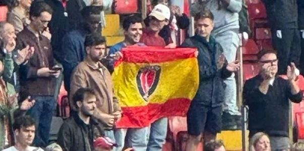 Group of fans holding a yellow and red flag with a central emblem.