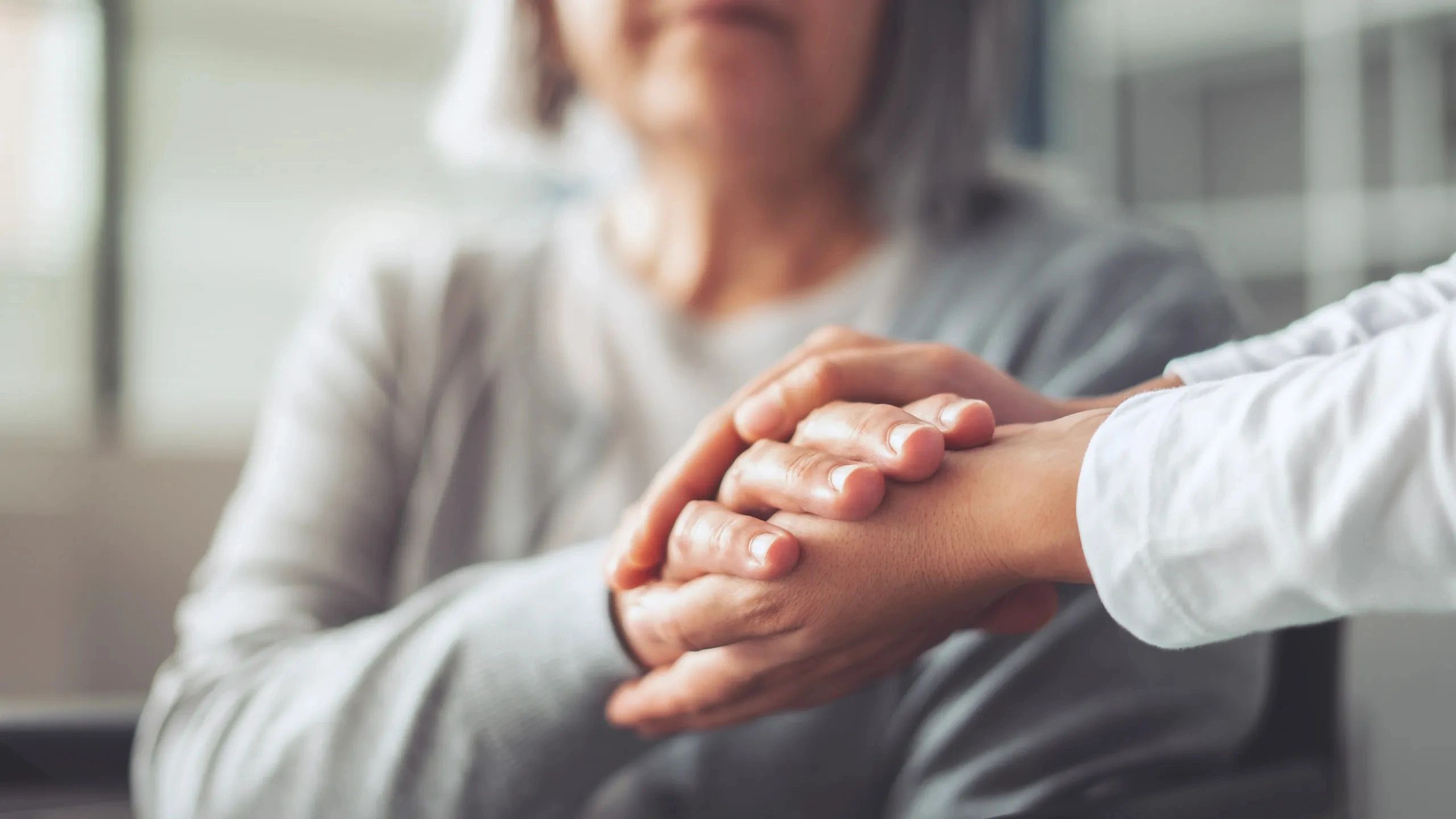 A person comforting an elderly individual by holding their hands.