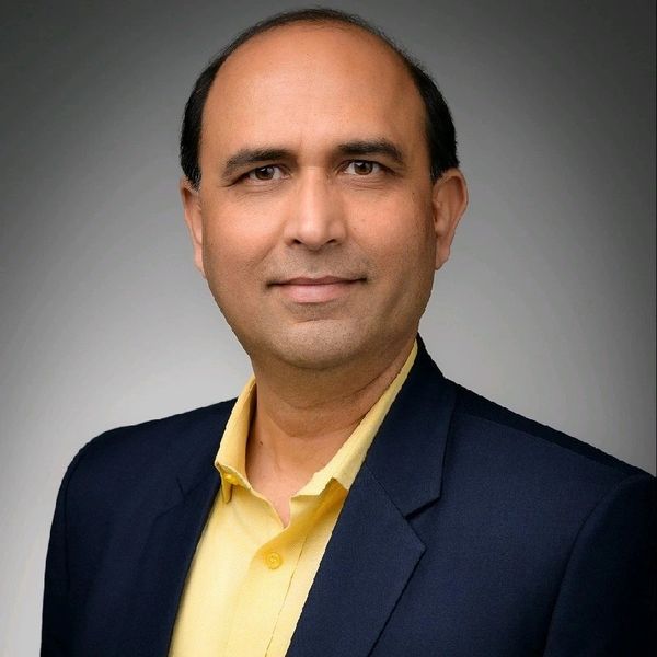 Professional headshot of a middle-aged man in a yellow shirt and dark blazer.