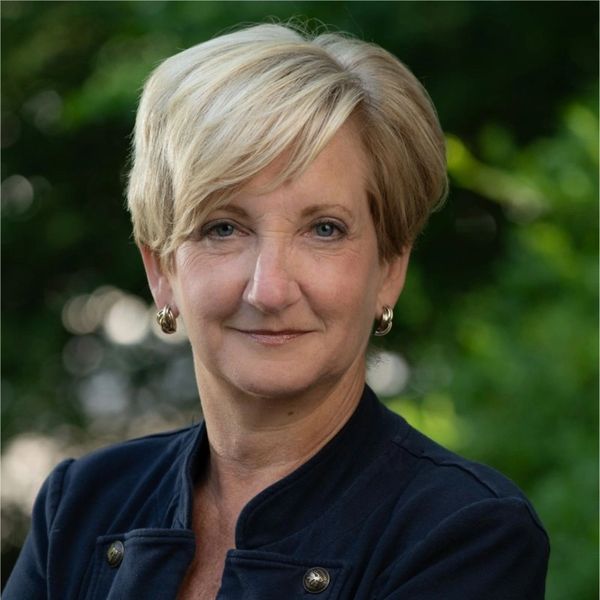 Confident middle-aged woman with short blonde hair in a dark blazer, posing outdoors.