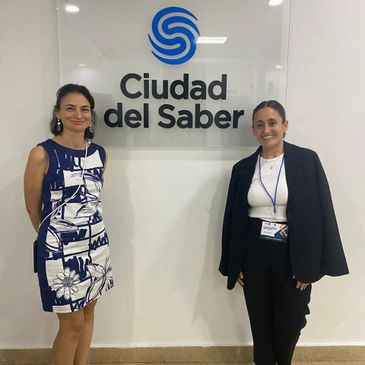 Two women standing beside a 'Ciudad del Saber' sign, smiling.