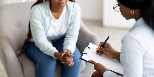 A woman attentively listens while another takes notes on a clipboard.